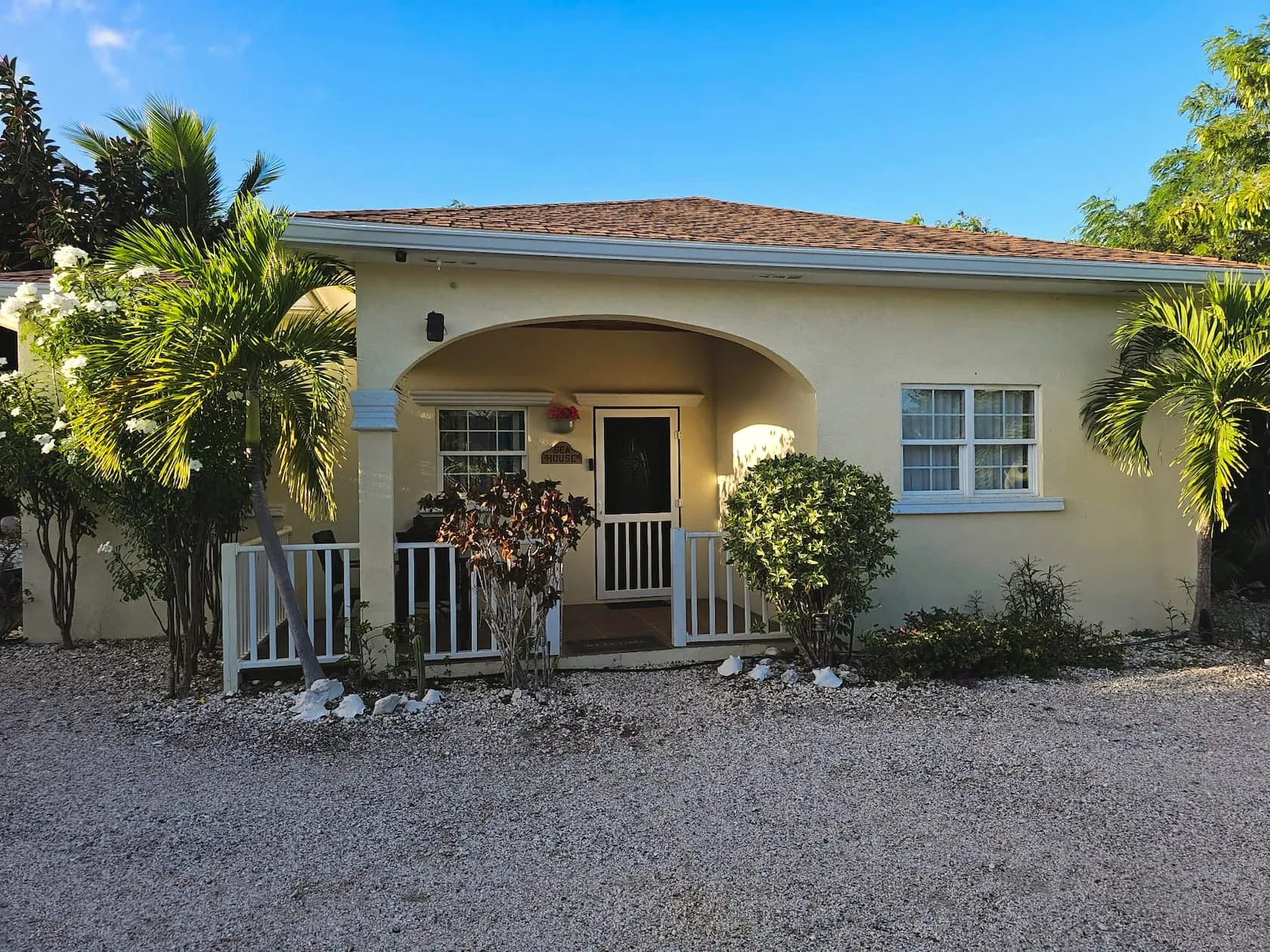 Front elevation of Sea Villa in morning light, with its arched porch, white railings, and shell-gravel drive