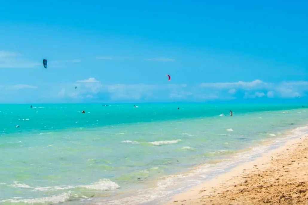 Long Bay shoreline with kites over the turquoise flats and a strip of warm sand
